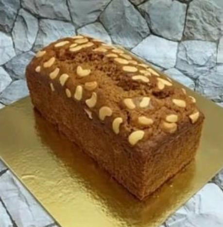 A carrot cake loaf topped with cashews on a gold board
